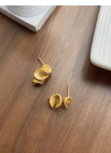 Detailed macro view of gold ruffled edge stud earrings with a matte brushed silver texture