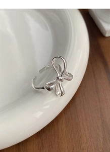 Close-up of minimalist S925 sterling silver bow ring on white ceramic plate surface