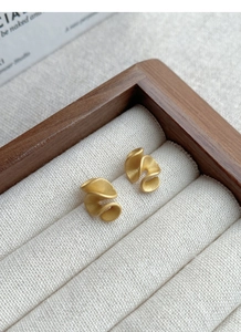 Macro detail of gold spiral earrings with a matte frosted finish in a jewelry display box