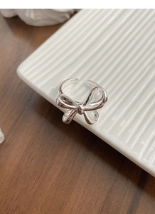Detail shot of a silver bow ring with twisted texture on a white ceramic display tray
