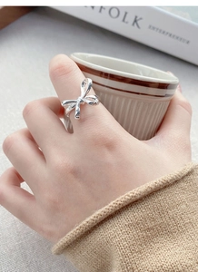 Close-up of a silver bow knot ring on a model's finger with a minimalist lifestyle background