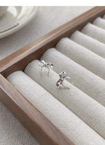 Detailed view of silver ribbon bow stud earrings placed in a wooden jewelry box display