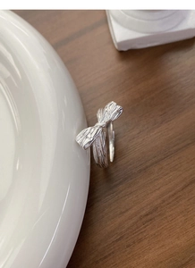 Detail of silver bow ring with irregular vintage texture on white ceramic plate
