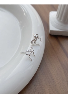 Detailed view of polished silver ribbon bow stud earrings on a white ceramic tray