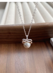 Macro d'un collier pendentif perle et nœud argenté dans un écrin à bijoux en bois