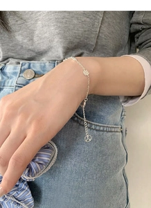 Detail of silver S925 bracelet on wrist with flower charm and peace sign pendant