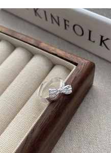 Detailed view of an irregular S925 sterling silver bow ring on a beige velvet jewelry box