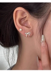 Close-up showing the elegant silver ribbon bow stud and white pearl earring on ear
