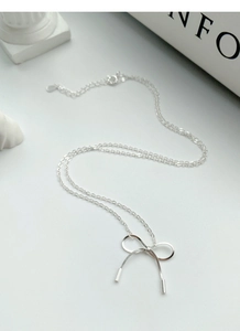 Detailed view of S925 silver bow pendant necklace with elegant metal tassels on white desk