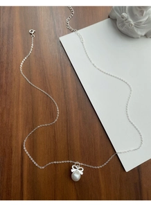 Détail du collier noeud en argent S925 avec perle sur surface boisée et décor en plâtre