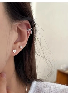 Close-up of S925 silver ribbon bow ear cuff and heart stud earring set on ear