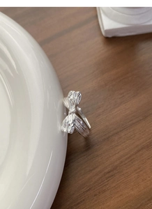 Macro detail of silver S925 bow ring with embossed texture on ceramic dish display