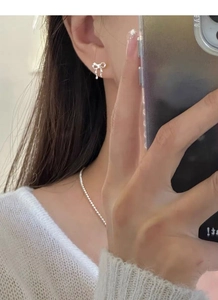 Detailed view of silver bow-shaped studs and beaded necklace on a model