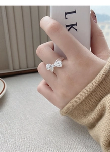 Detailed close-up of a silver bow ring with a brushed texture finish on a finger