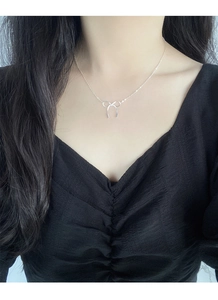 Close-up of S925 silver bow necklace on a model wearing a black V-neck dress