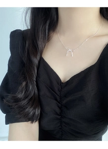 Detailed close-up of a silver bow pendant necklace worn by a model on a dark background