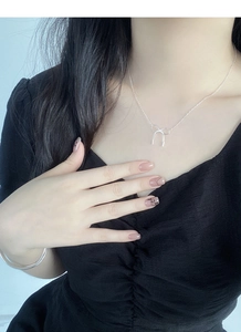Close-up of S925 silver bow pendant necklace worn by a model on a black V-neck dress