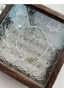 Detail of S925 silver bracelet with green jade beads and lotus charm on glass tray