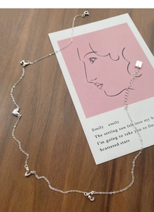 Detail of silver S925 necklace with heart, music note and letter charms on a pink card