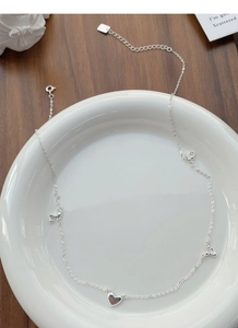 Detail of S925 silver necklace with heart and letter pendants on a ceramic plate