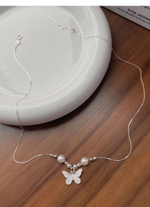 Detailed view of S925 silver butterfly necklace with elegant pearls on a ceramic dish