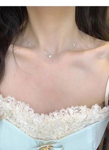 Detail of S925 silver heart necklace with V and J letter charms on female model neck