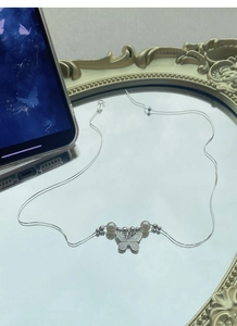 Detailed close-up of S925 sterling silver butterfly necklace with white pearls on a mirror