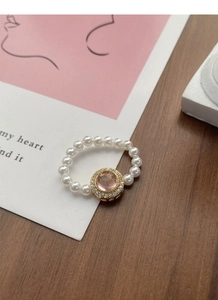 Detailed macro view of pink gemstone ring with white pearls on a vintage wooden surface