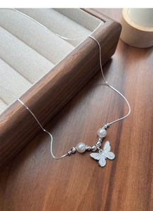 Detailed close-up of a silver butterfly pendant with white pearls on a sleek box chain