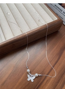 Macro detail of silver butterfly pendant with elegant white pearls on a fine metal chain