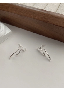 Dettaglio orecchini a nastro argentati su sfondo minimalista bianco con legno