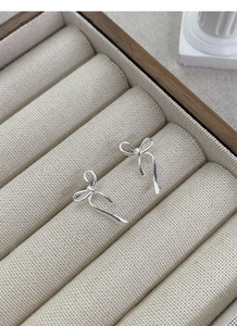 Dettaglio degli orecchini a fiocco in argento S925 su scatola portagioie beige strutturata