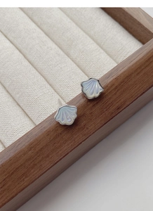 Detailed view of S925 silver seashell earrings with pearlescent finish on a soft cushion