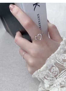 Detailed view of silver hollow heart ring and textured band worn on hand over book