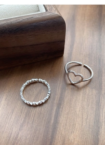 Close-up of hollow heart and linked heart silver rings on a natural wooden table