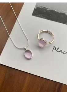 Detailed view of silver necklace and ring set with oval pink gemstones on wood base