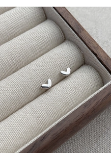 Close-up of small silver heart stud earrings resting in a wooden jewelry display box