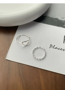 Flat lay of S925 sterling silver hollow heart ring and textured band on wooden desk