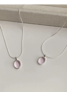 Detailed view of silver necklaces with pink oval gemstone pendants on a minimal background