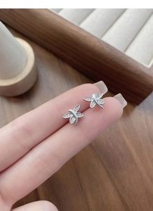 Macro detail of silver dragonfly stud earrings with white zircon accents held on fingertip