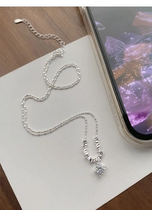 Detailed macro view of S925 sterling silver bead chain with zircon pendant on white paper