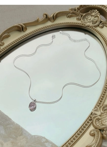 Macro detail of a pink oval pendant necklace displayed on a vintage gold mirror