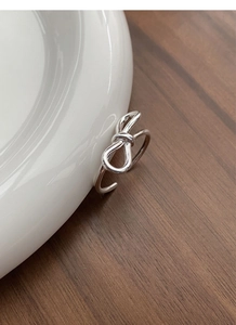 Close-up of minimalist silver bow ring on white porcelain edge with wood background