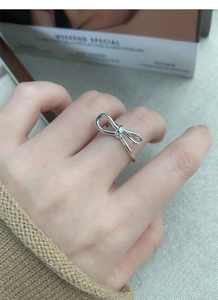 Detail of a minimalist silver bow ring on a finger with a warm winter sweater