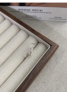 Close-up of minimalist S925 sterling silver bow ring on a natural linen jewelry box