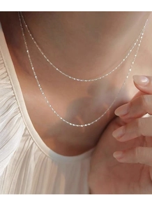 Close-up of layered S925 sterling silver necklaces on neck with white blouse