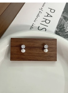 Detail view of S925 silver square zircon and freshwater pearl stud earrings on a wooden base