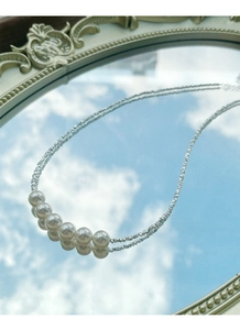 Macro view of silver necklace with seven white pearls reflected on a mirror against blue sky