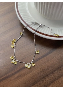 Detail of adjustable silver beaded bracelet with yellow teardrop zircon charms on table