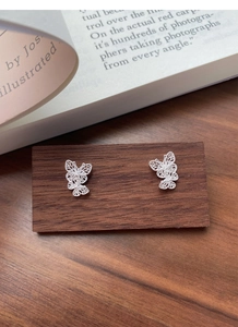 Macro shot of silver filigree butterfly stud earrings on a dark wood and book background